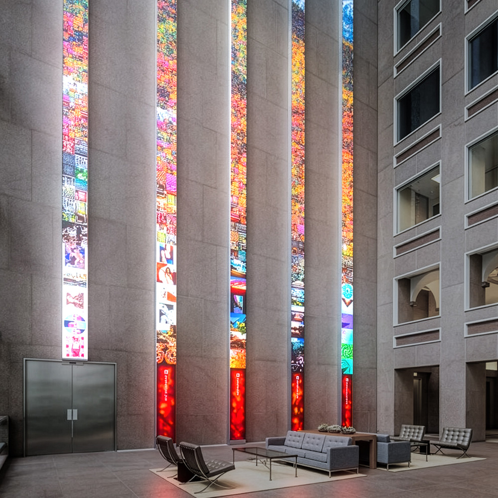 Referencia: columnas verticales de pantallas LED con visuales de colores en un hall de piedra
