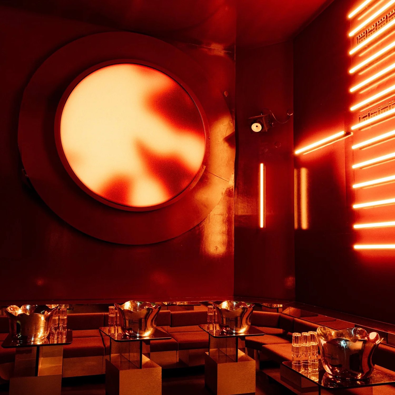 Referencia: círculo luminoso naranja en una pared roja con tubos de neón sobre un reservado de bar
