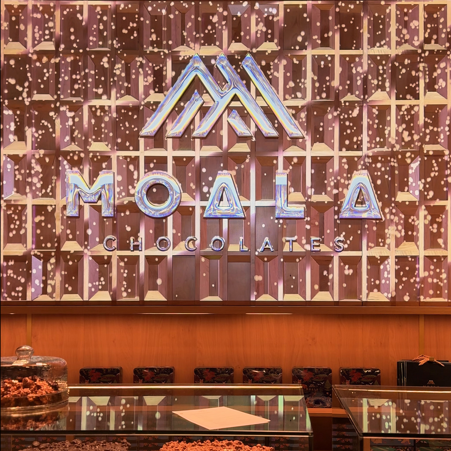 Logo Moala Chocolates proyectado en revestimiento de madera, efecto nevado